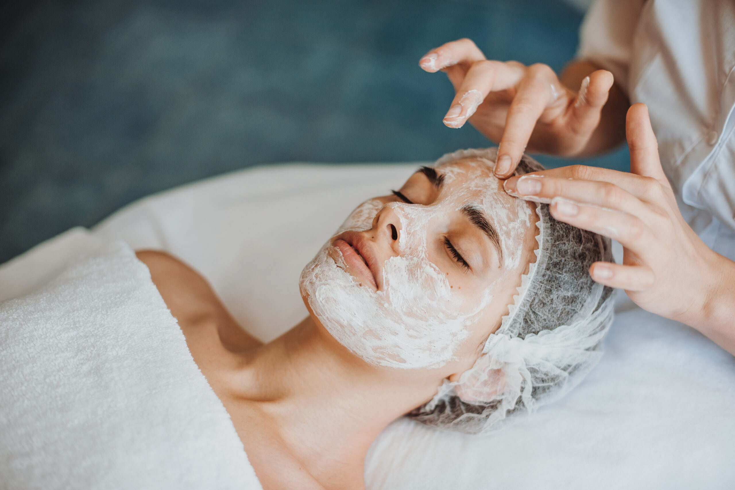 Woman face getting facial care with cream by beautician hands at spa salon. Close-up portrait.