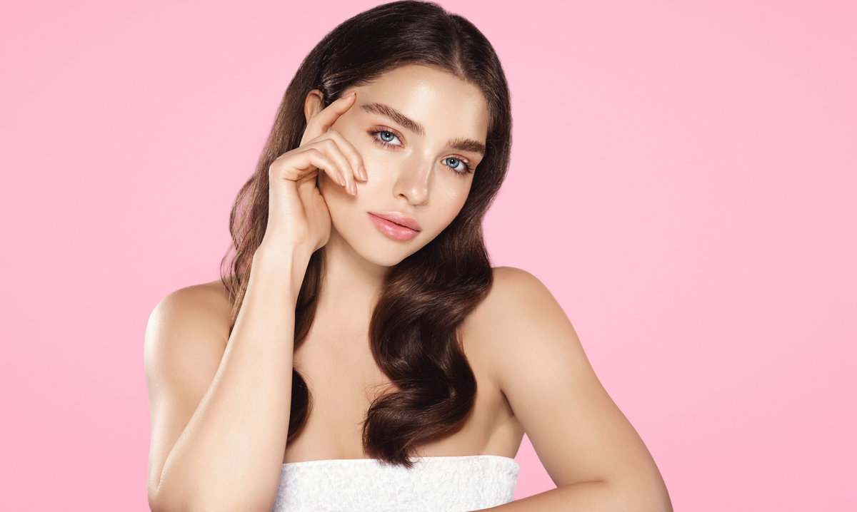 Beauty. Woman 25 years, has shiny glowing skin, clean nourished body and face, looks sensual at camera, eyebrows sick with brow gel, pink background.