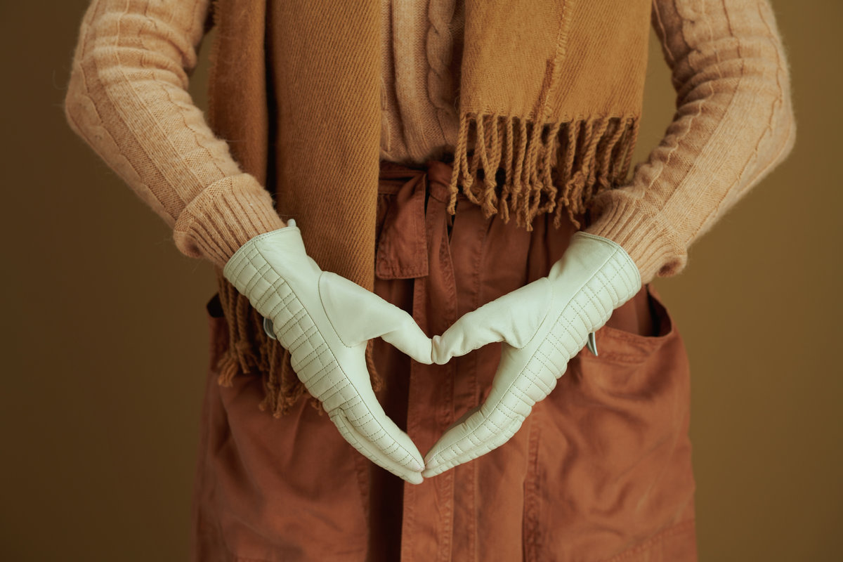 Hello autumn. Closeup on middle aged woman in scarf with leather gloves showing heart shaped hands isolated on beige background.
